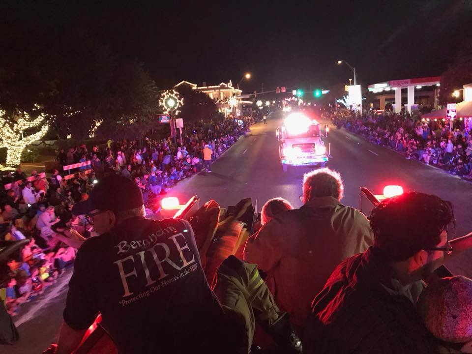 A group of people are watching a fire truck parade at night.
