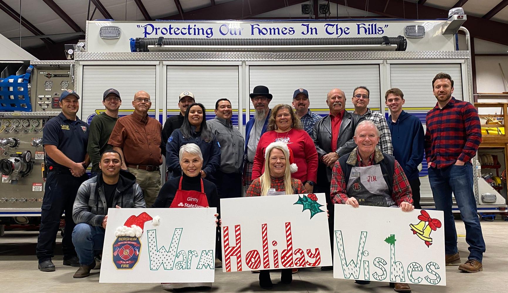 A group of people are standing in front of a fire truck holding signs that say warm holiday wishes.