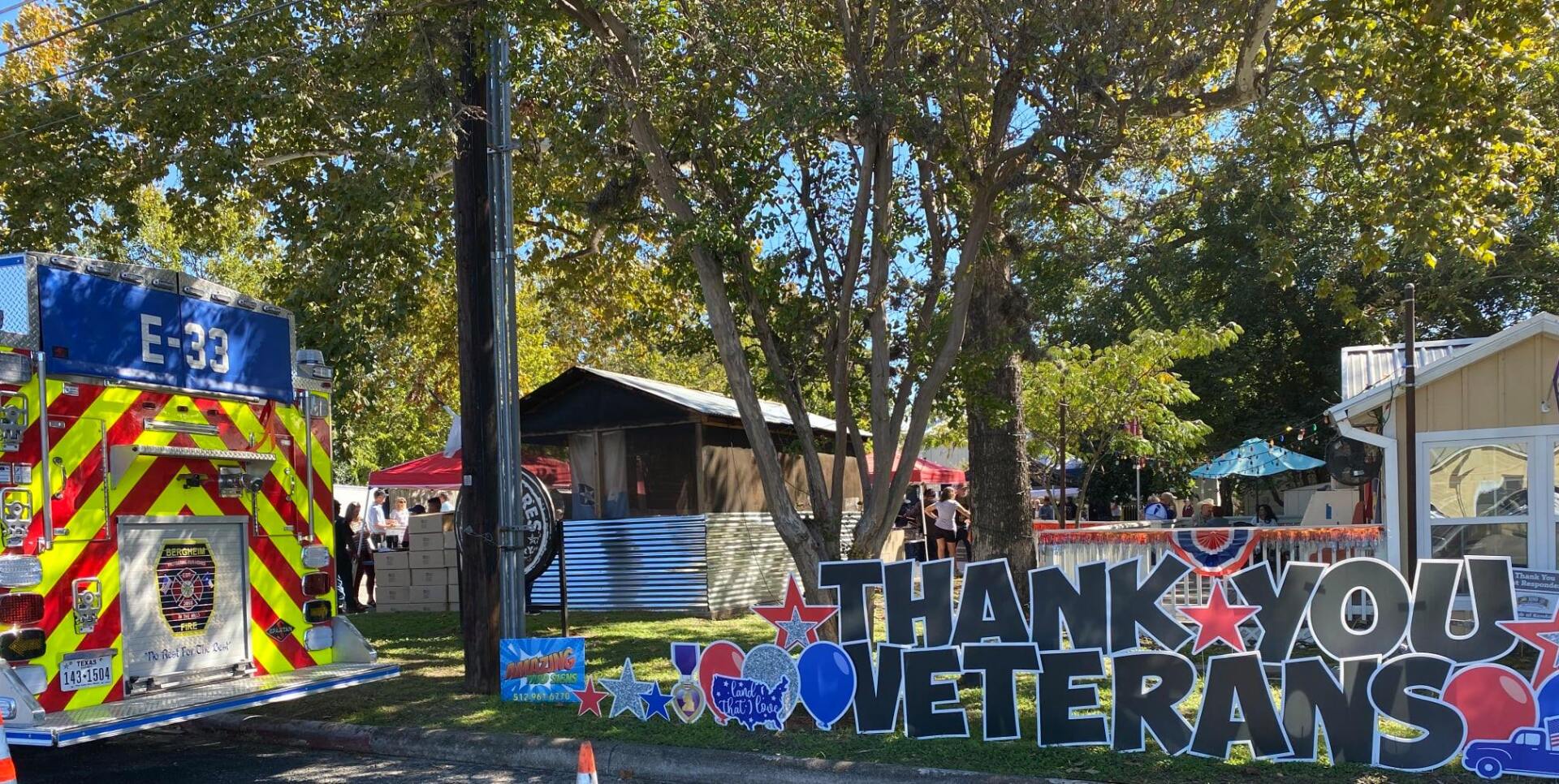A fire truck is parked in front of a sign that says `` thank you veterans ''.