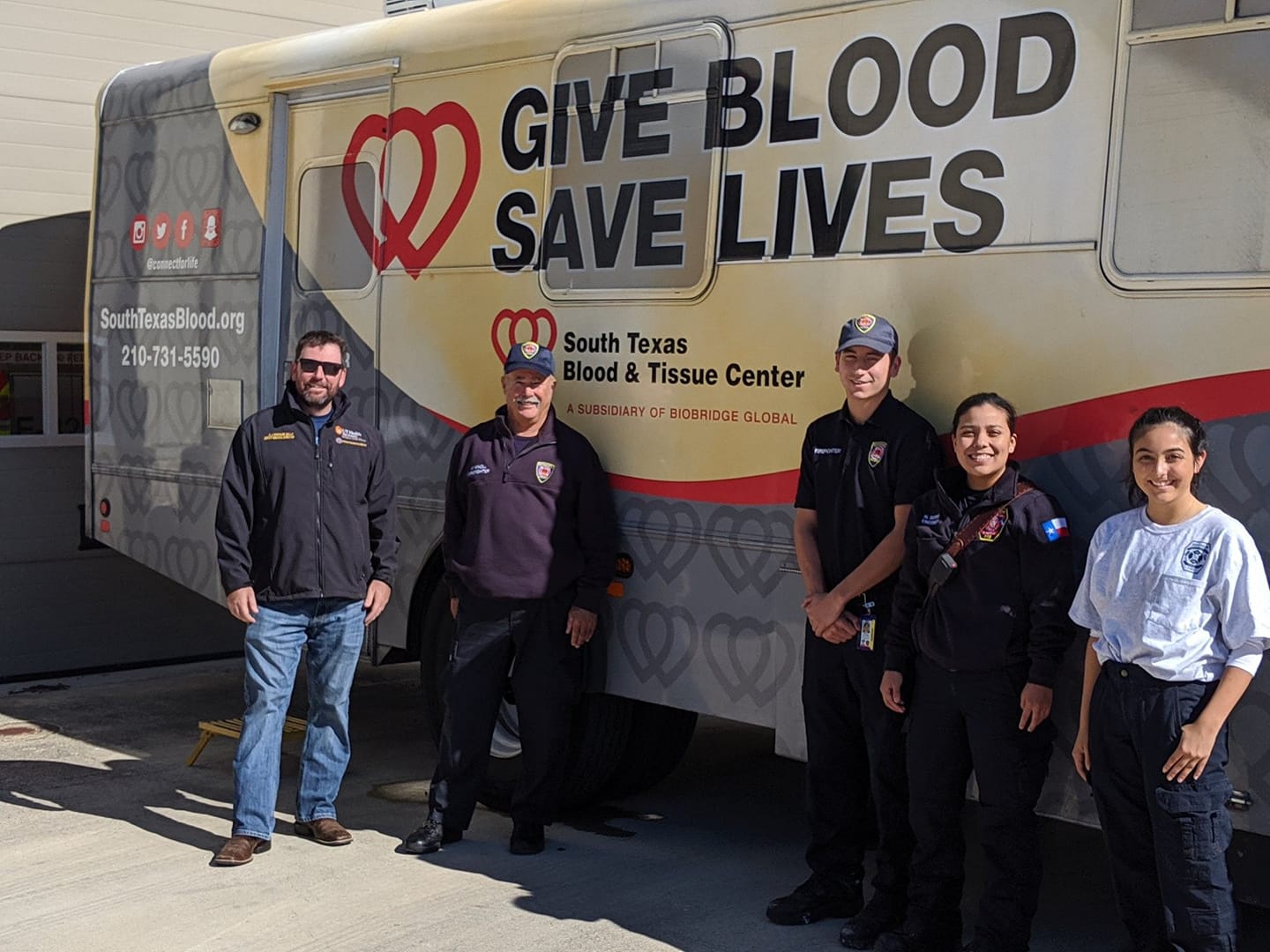 A group of fire fighters are standing in front of a Blood Bank donation motor coach