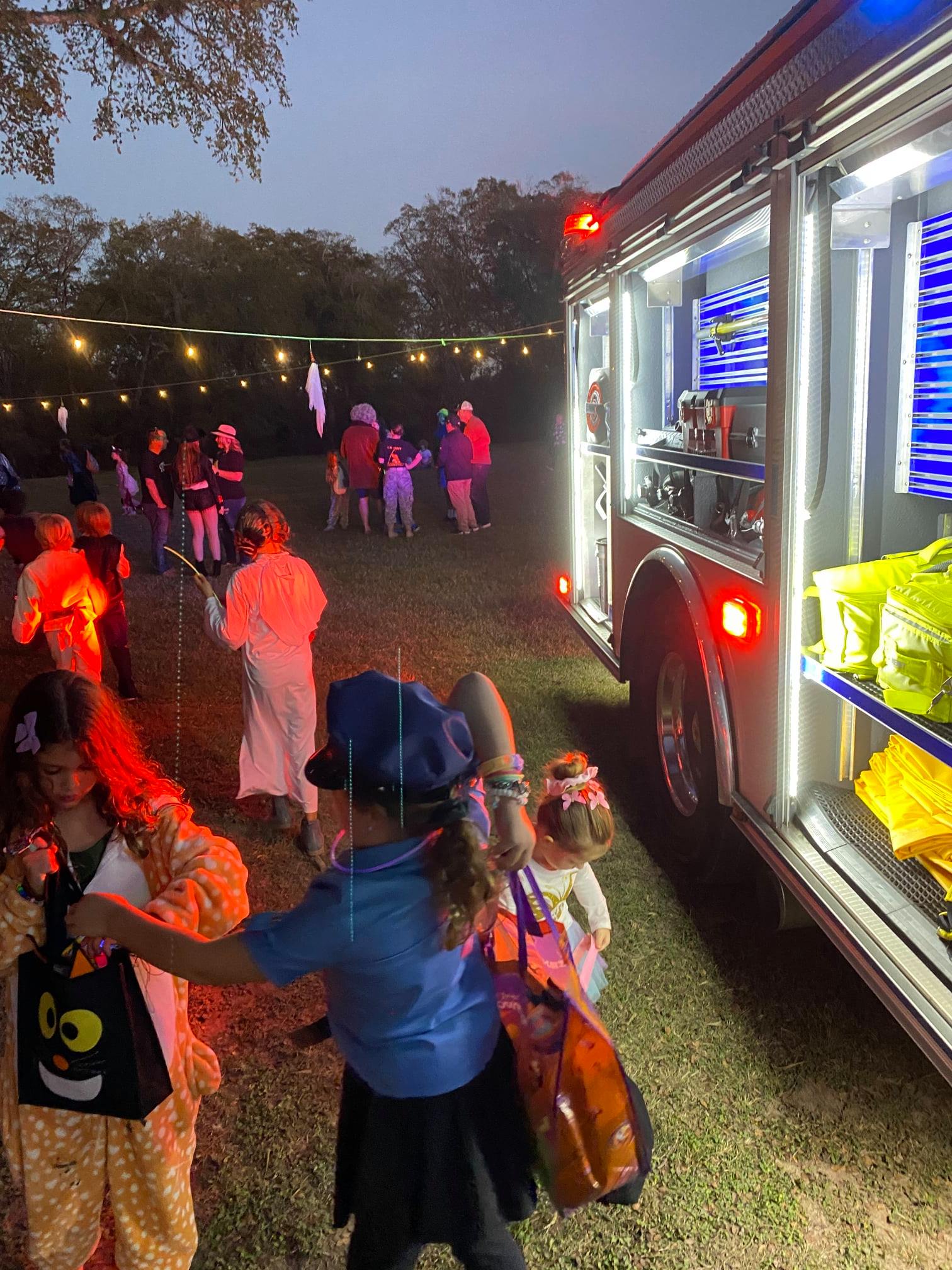 A group of children in costumes are standing in front of a fire truck.