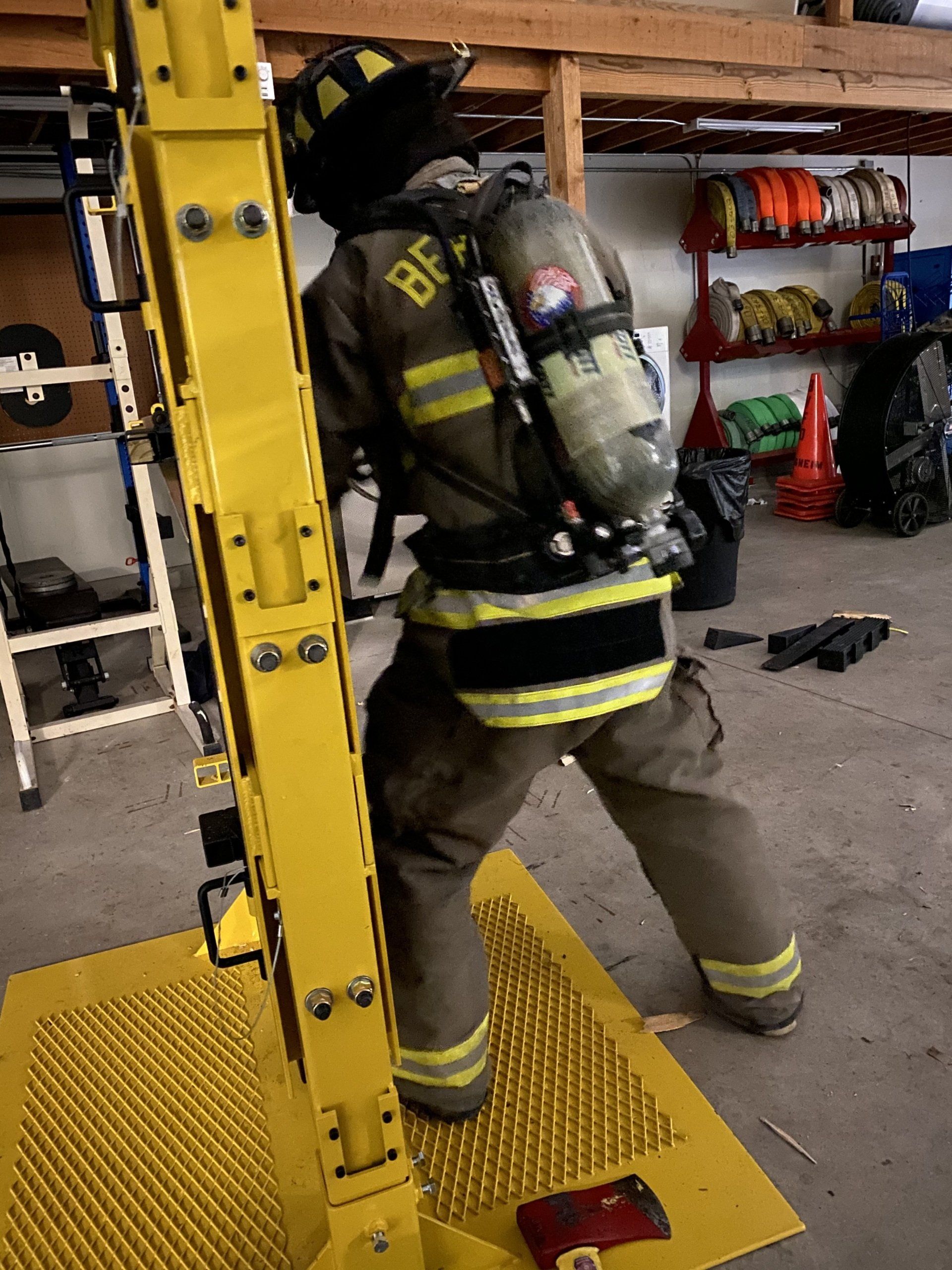 A fireman wearing a helmet and oxygen tank is training on how to breach a door.