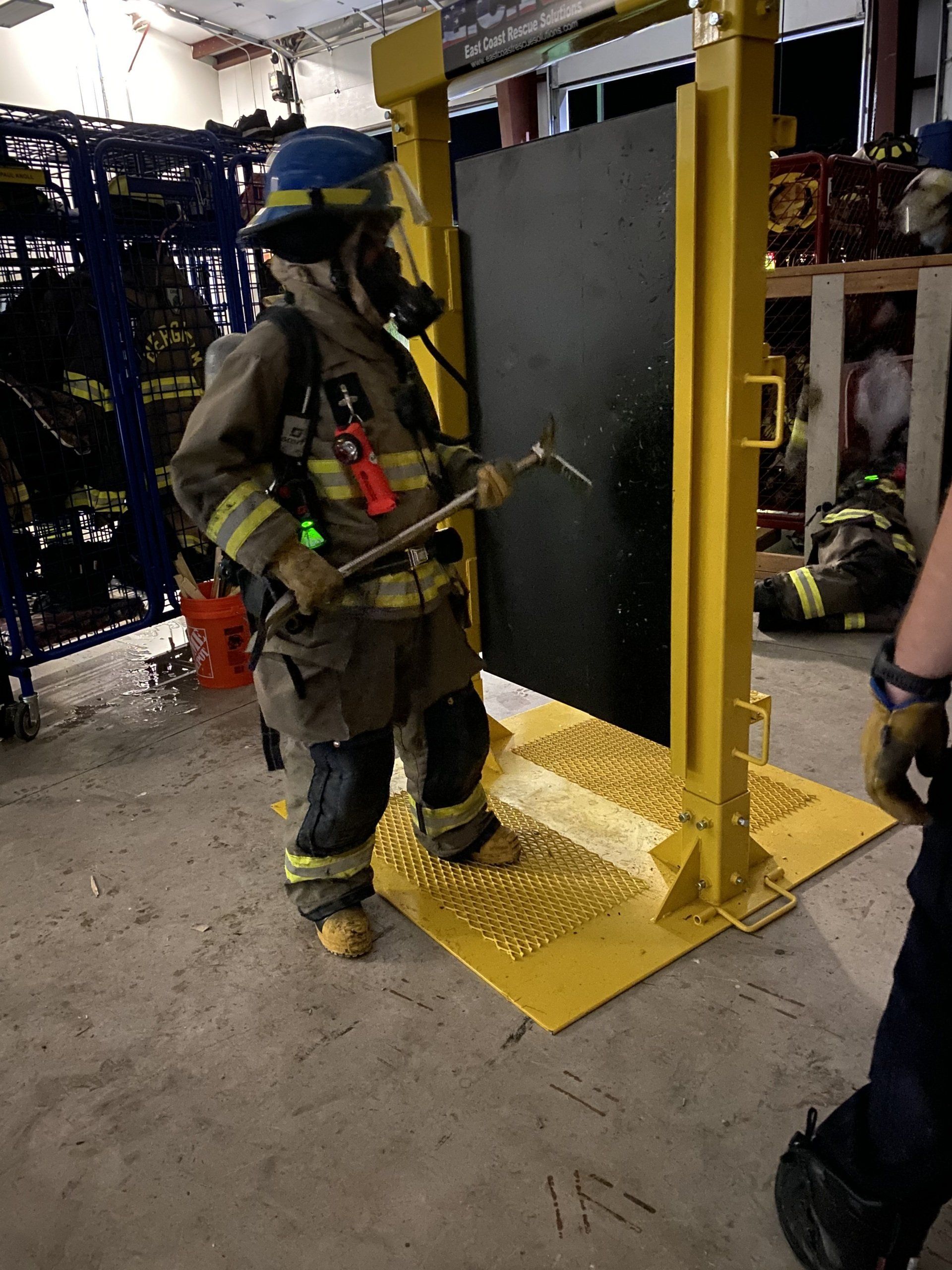 A fireman wearing a helmet and oxygen tank is training on how to breach a door.