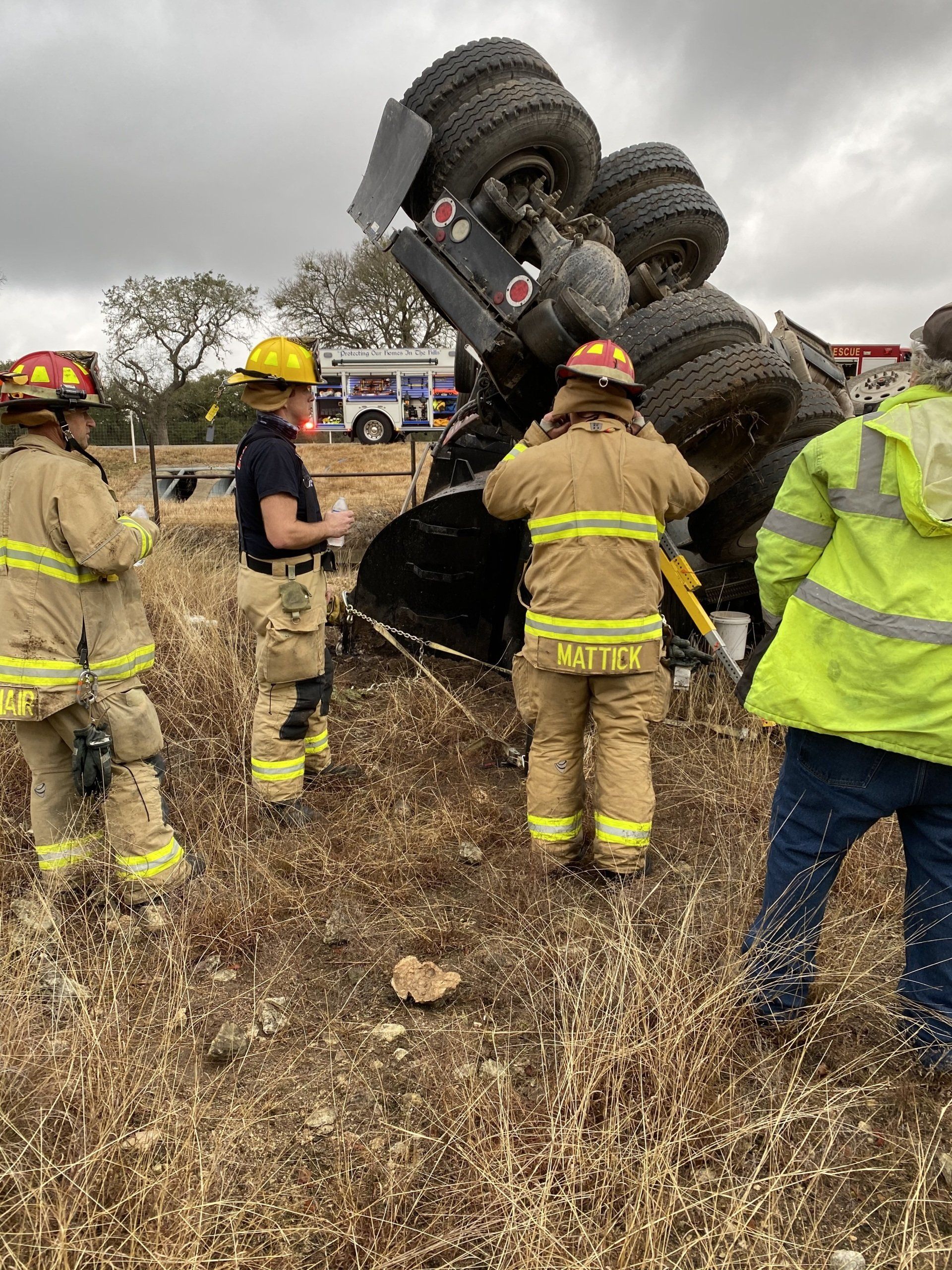 A group of firefighters are standing in a field next to a truck that has rolled over.
