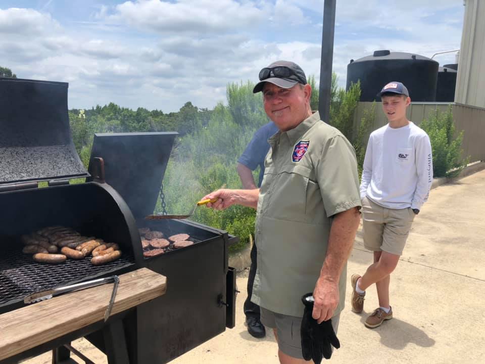 A man is cooking food on a grill while a boy watches for a fire department fund raiser.
