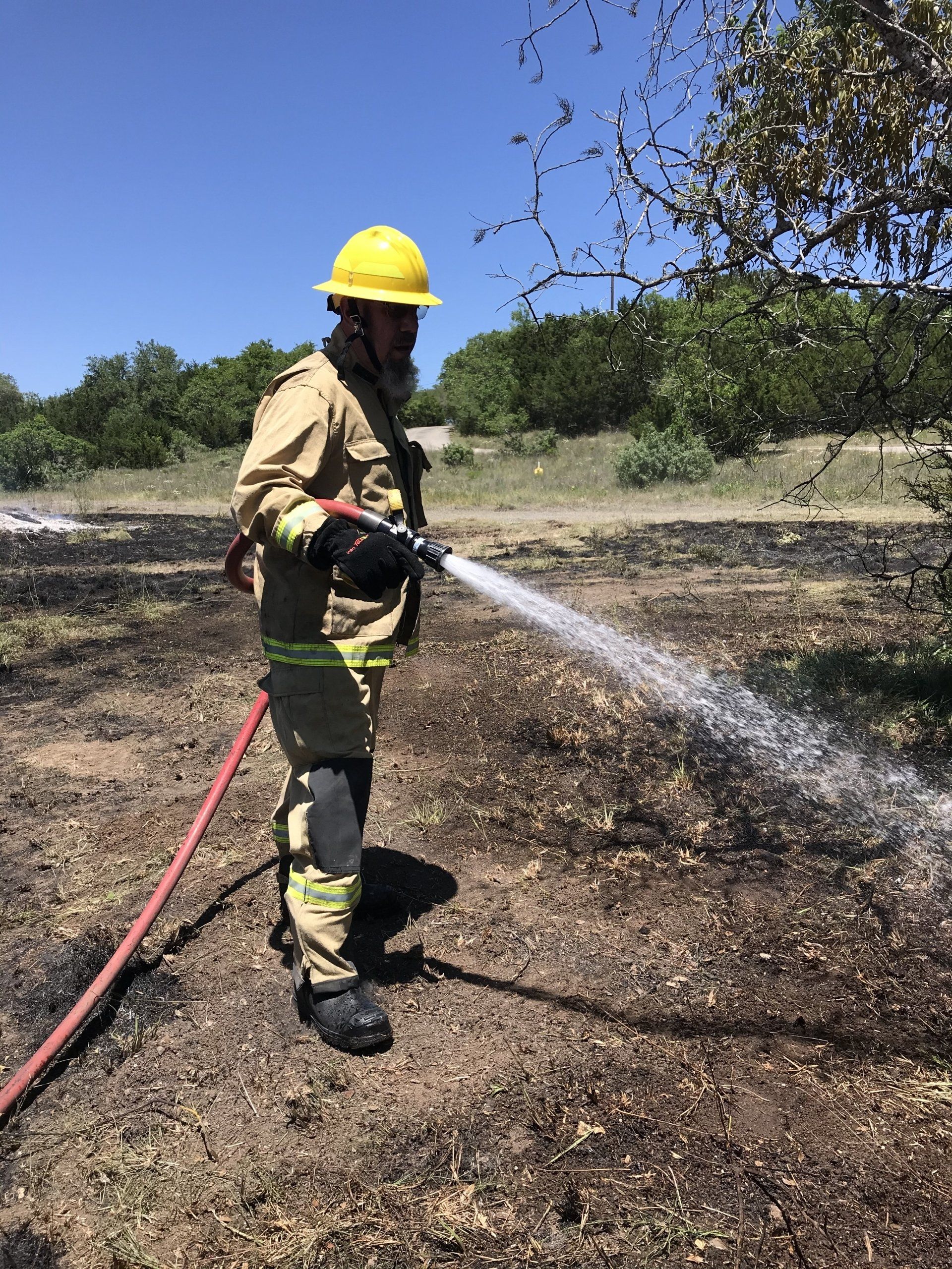 A firefighter is spraying water from a hose on a field.