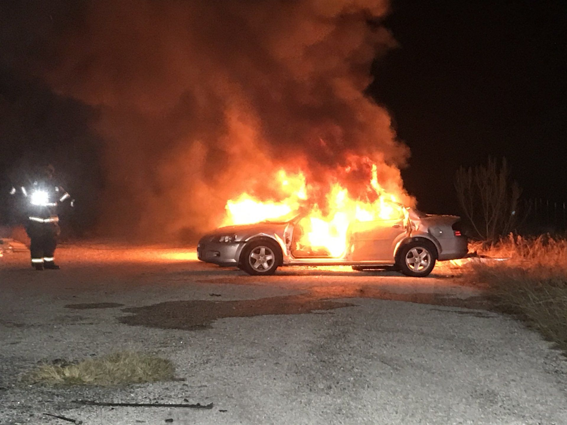 A vehicle is on fire with a fire fighter approaching