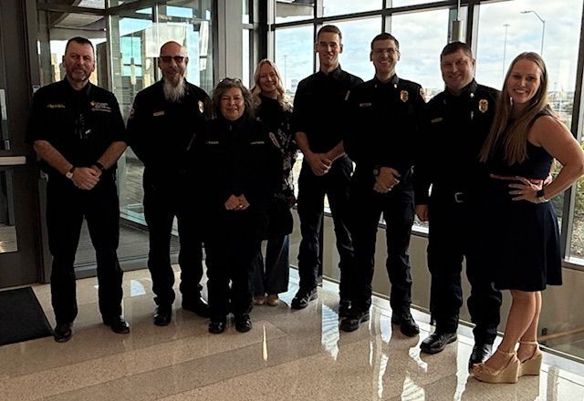 Group of people, including individuals in dark uniforms, posing indoors near a window.
