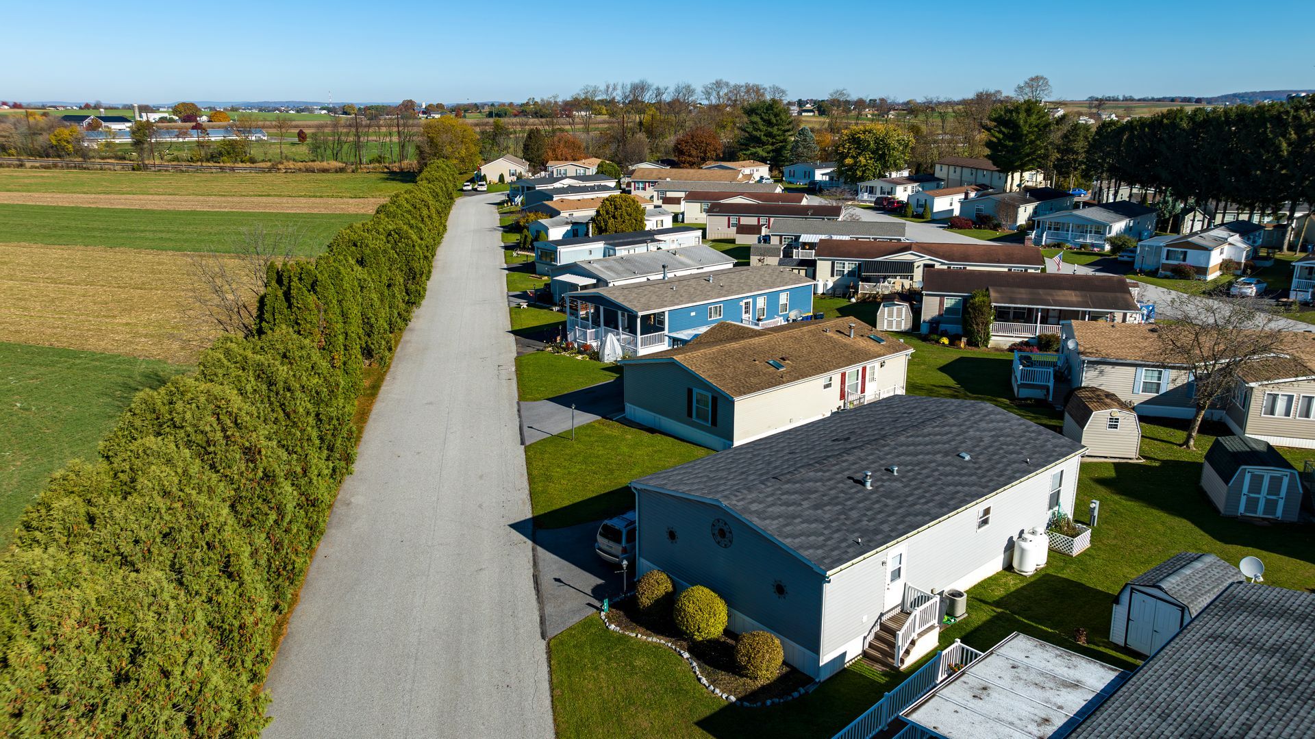 Aerial view of suburban homes beside a long road and open fields on a sunny day