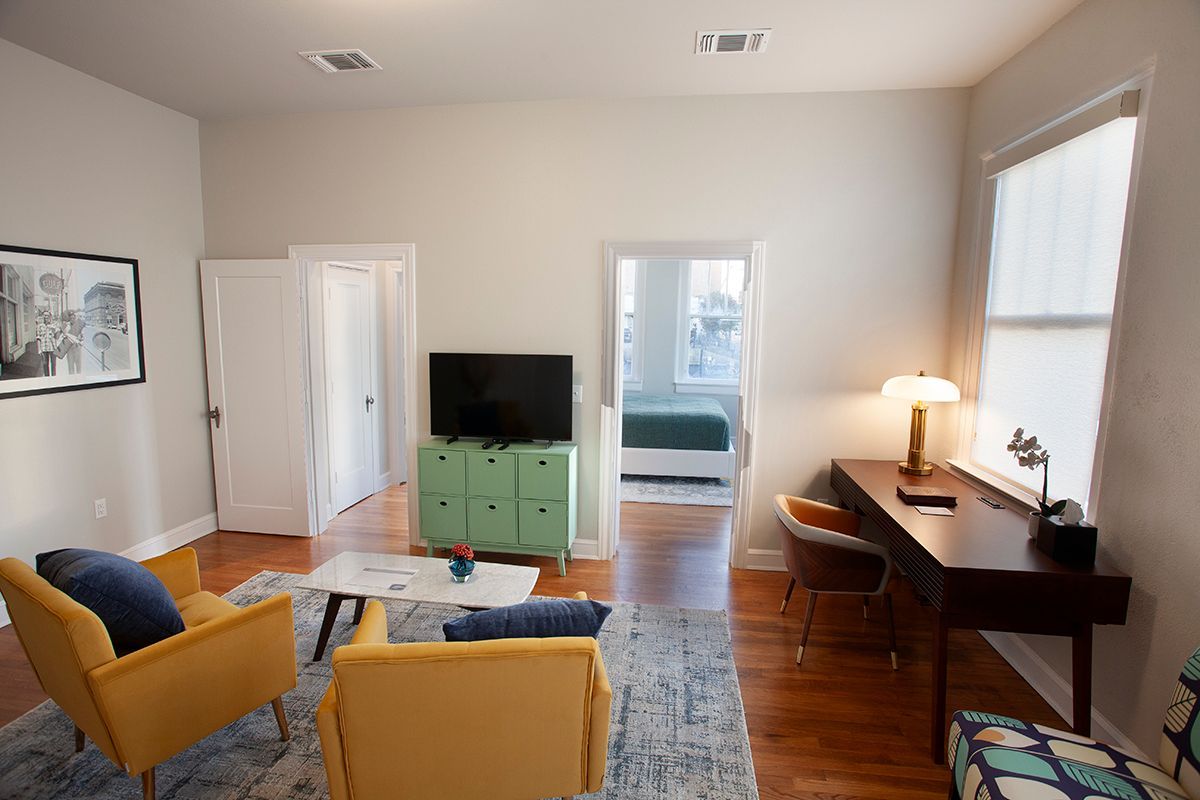 A living room with yellow chairs , a desk and a flat screen tv.