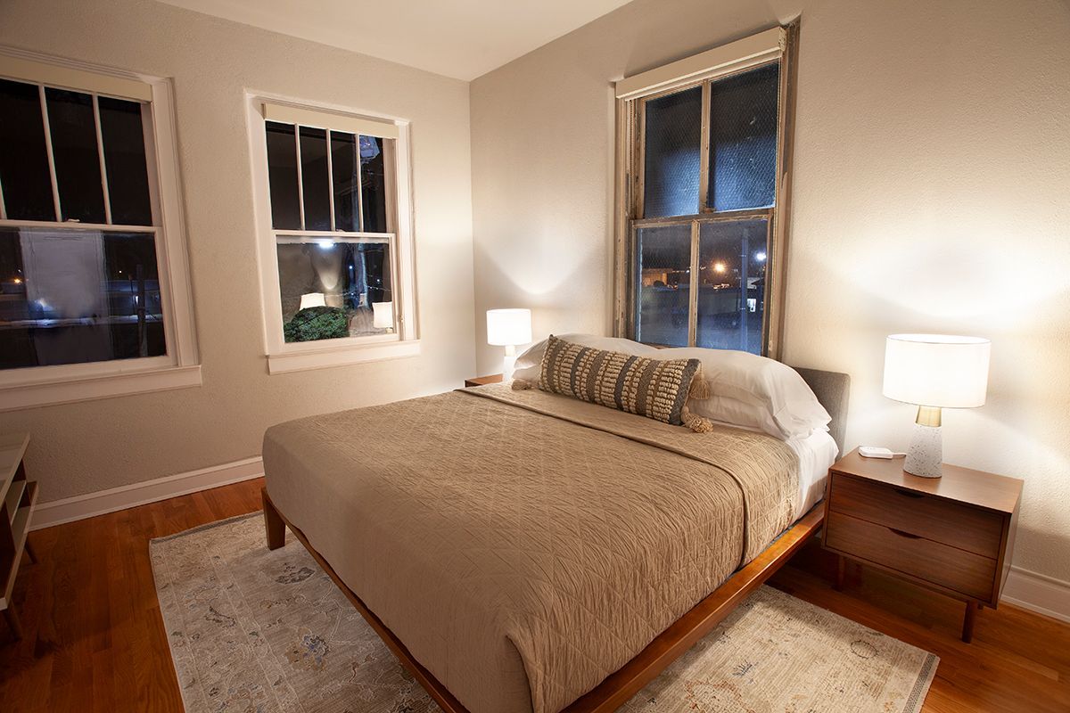 A bedroom with a bed , nightstand , and two windows.