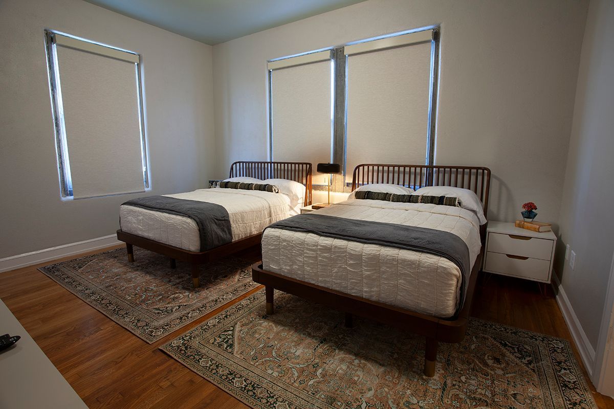 A bedroom with two beds , two nightstands and two windows.