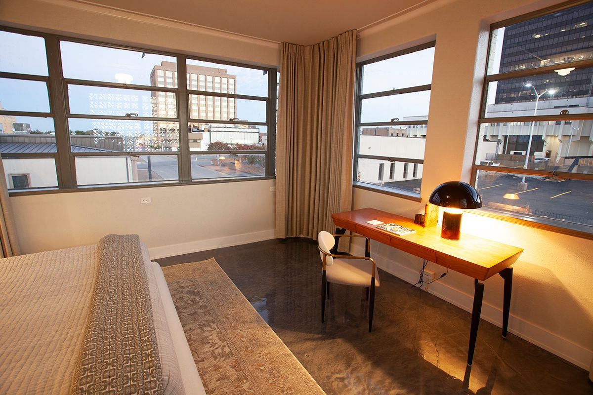 A bedroom with a bed and a desk with a lamp on it