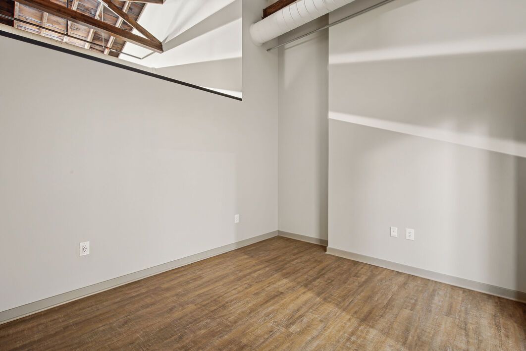 Empty room with light gray walls, wood-look floor, and exposed ceiling beams.