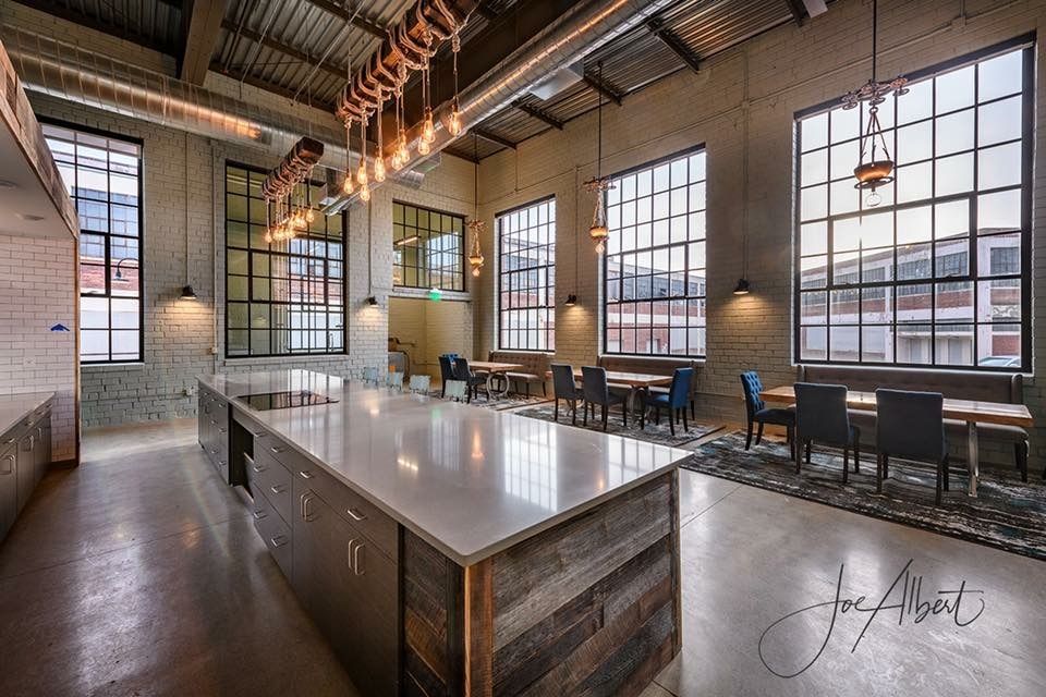 Modern kitchen and dining area in a loft with large windows, concrete floors, and a large island.