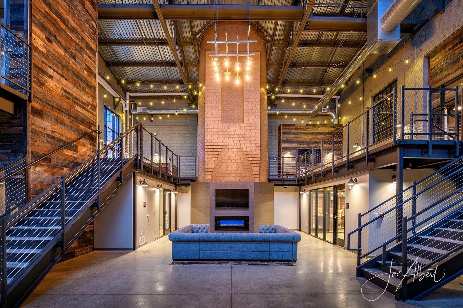 Modern industrial-style lounge with brick fireplace, metal staircases, and a blue sofa.