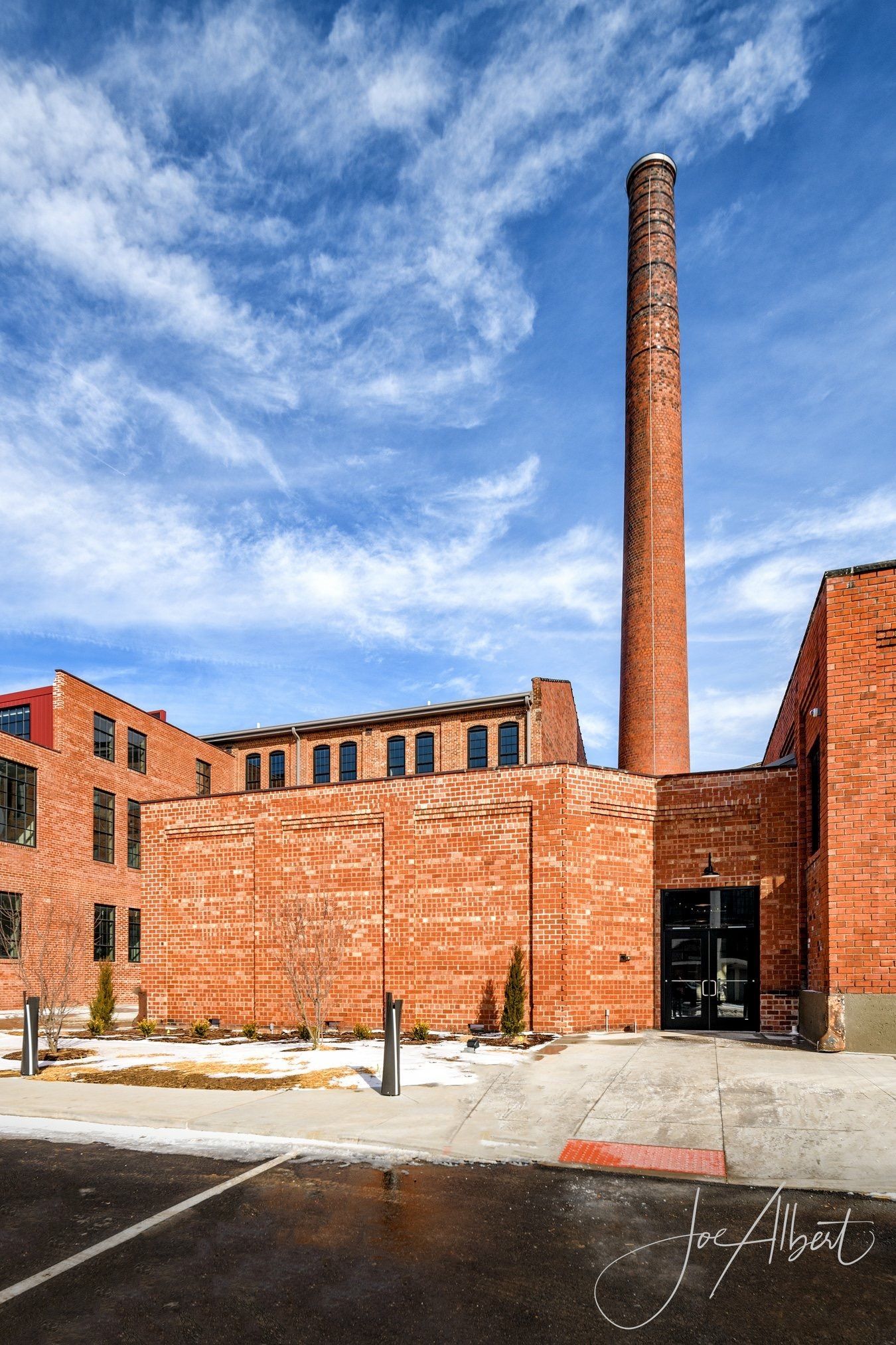 Brick industrial building with tall smokestack against a blue sky with streaky clouds.