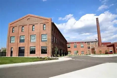Red brick industrial building with a tall smokestack on a sunny day.