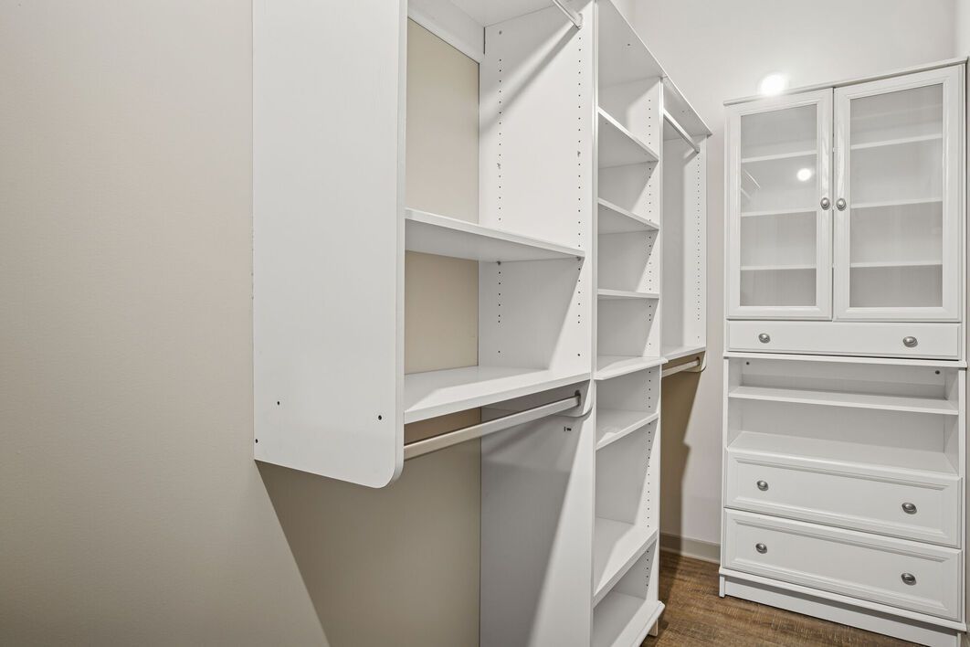White closet with shelves, drawers, and glass-door cabinet in a room with hardwood flooring.