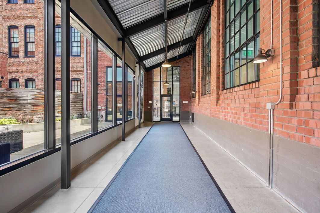 Hallway with blue carpet, exposed brick walls, and large windows.