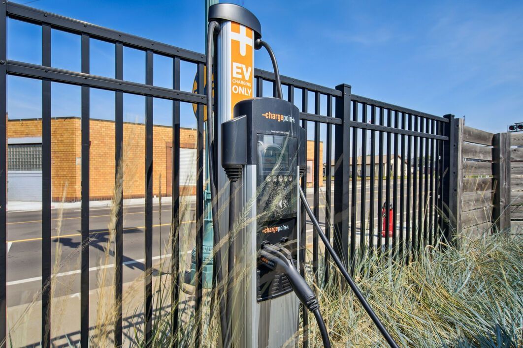 EV charging station next to a black fence, with a building in the background.