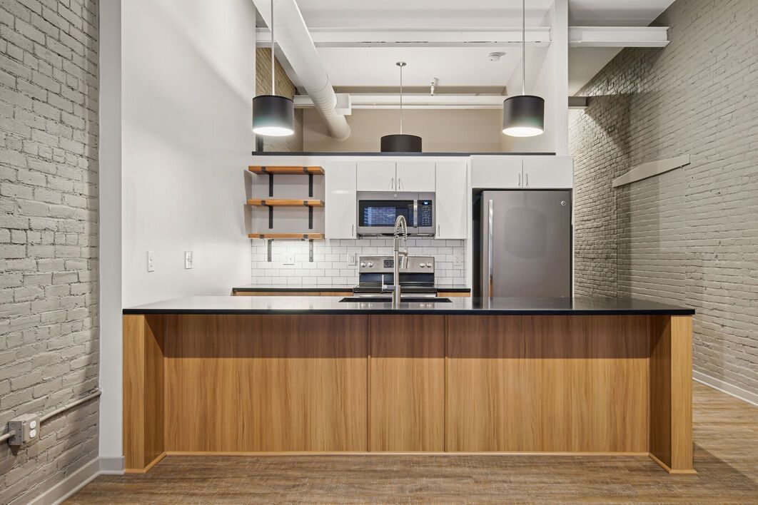 Modern kitchen with wood island, white cabinets, brick walls, stainless steel appliances, and hanging lights.
