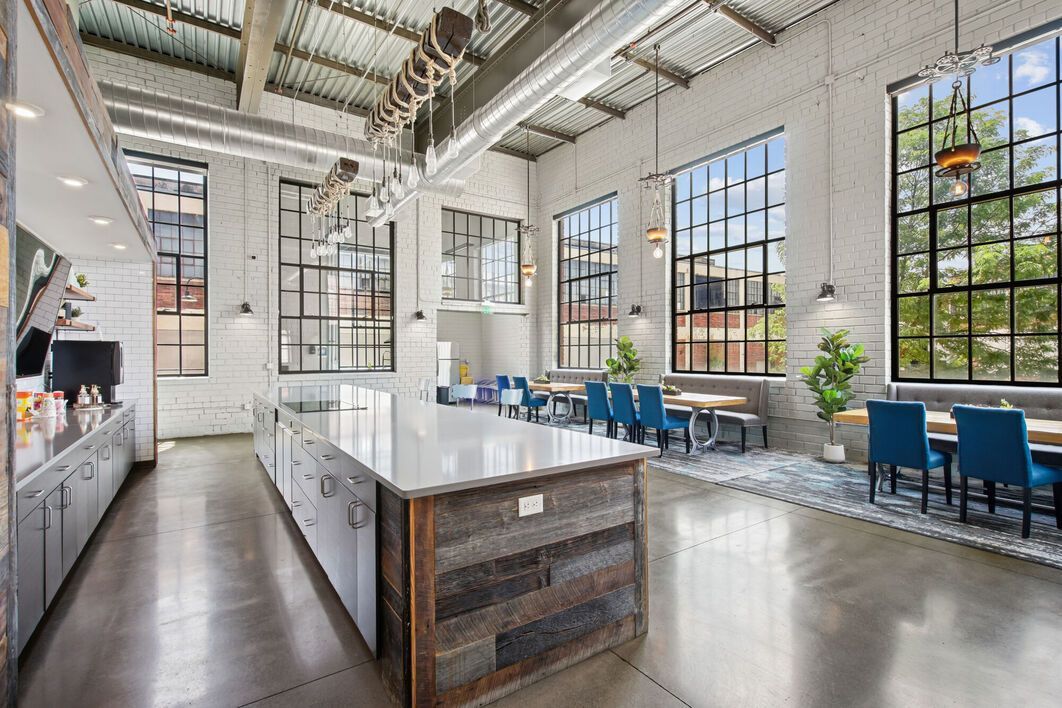 Modern, industrial-style kitchen with large windows, an island, and seating area. White brick walls, concrete floors.