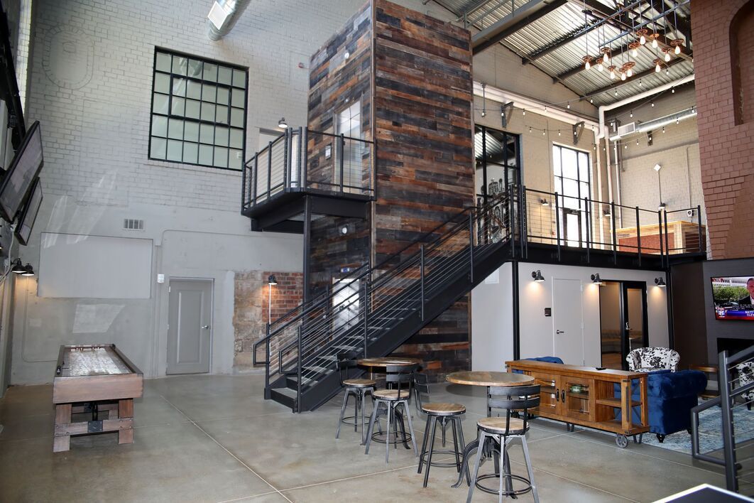Interior of a modern industrial-style space with a wooden elevator structure, staircase, bar seating, and open layout.