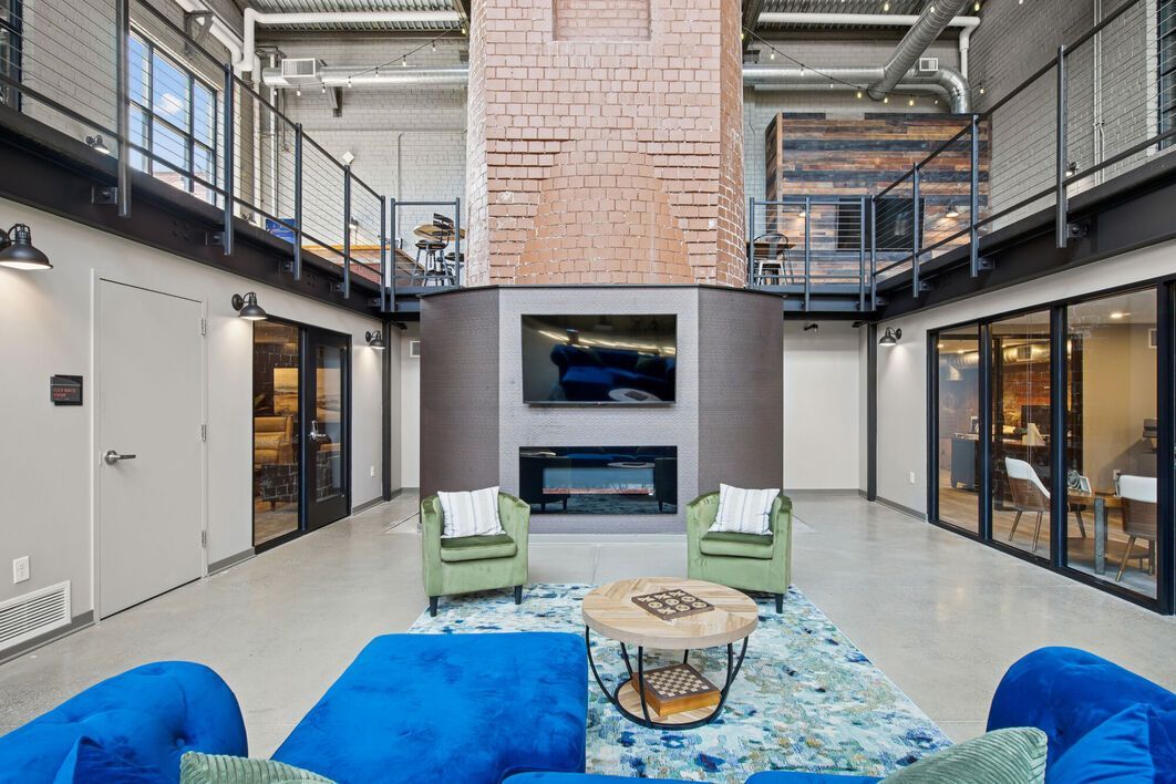 Lobby with fireplace, TV, and seating, featuring a blue couch, green armchairs, and a rug.