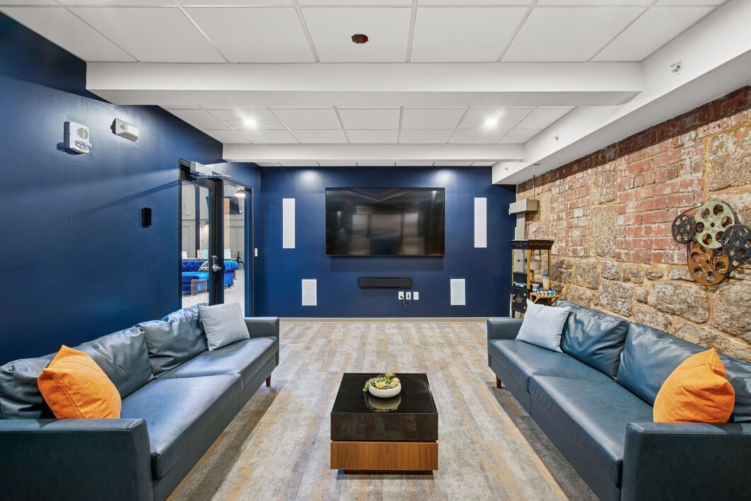 Modern lounge with blue walls, two couches, TV, and exposed brick.