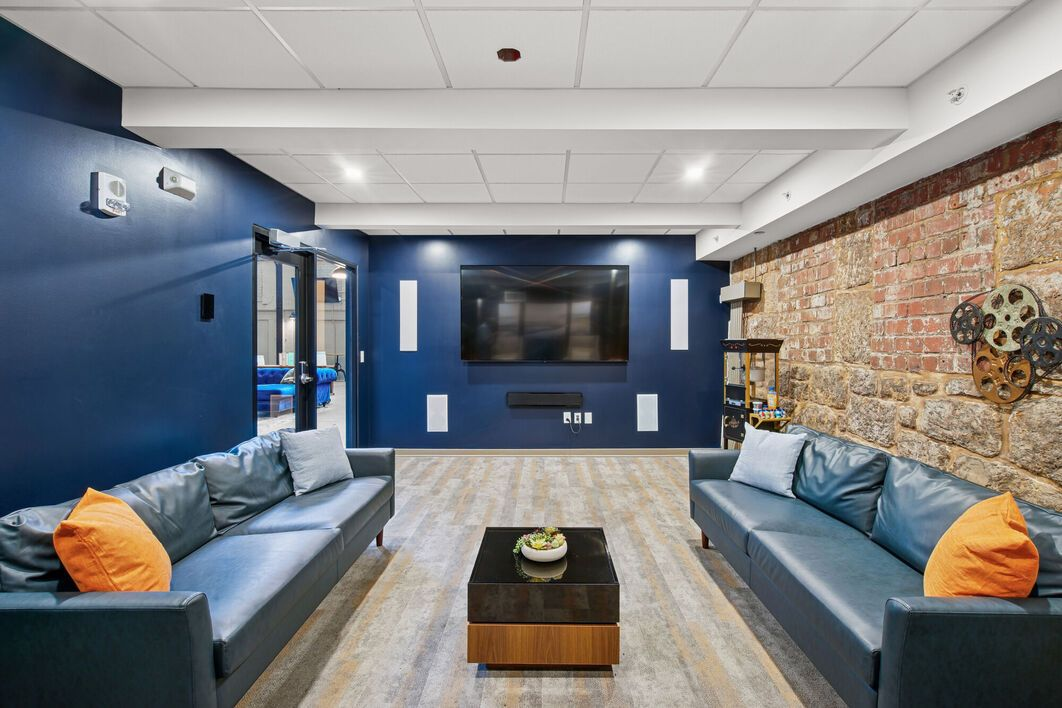 A modern lounge area with navy blue walls, two couches, and a large TV. A brick wall is visible on the right.