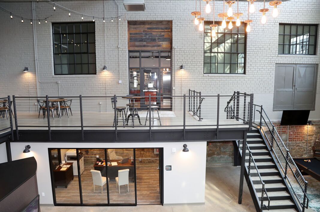 Two-story office interior with exposed brick and metal accents, overlooking a lower-level office space with a staircase.