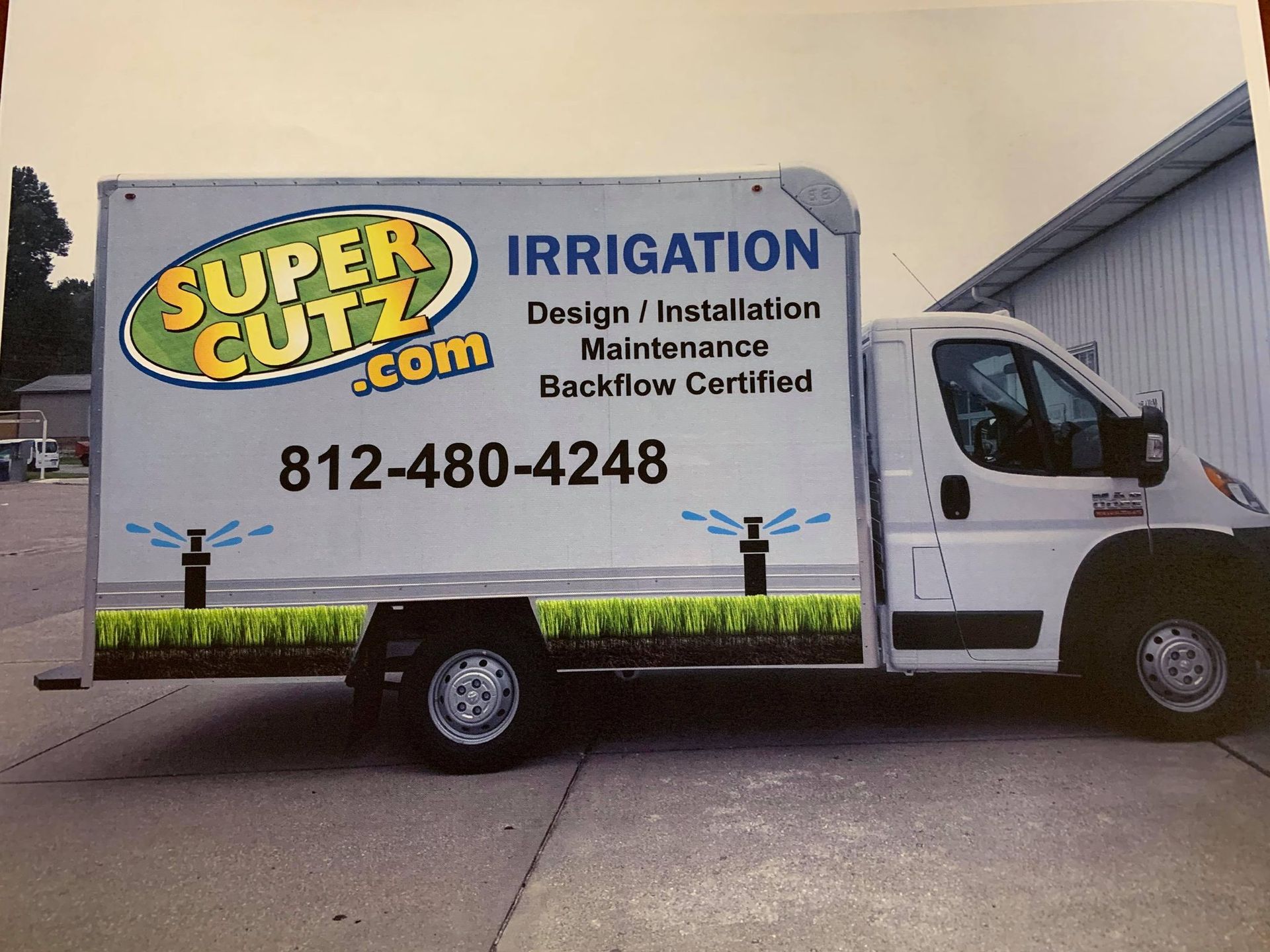 White Super Cutz truck with logo and irrigation details, including a phone number, parked outside.