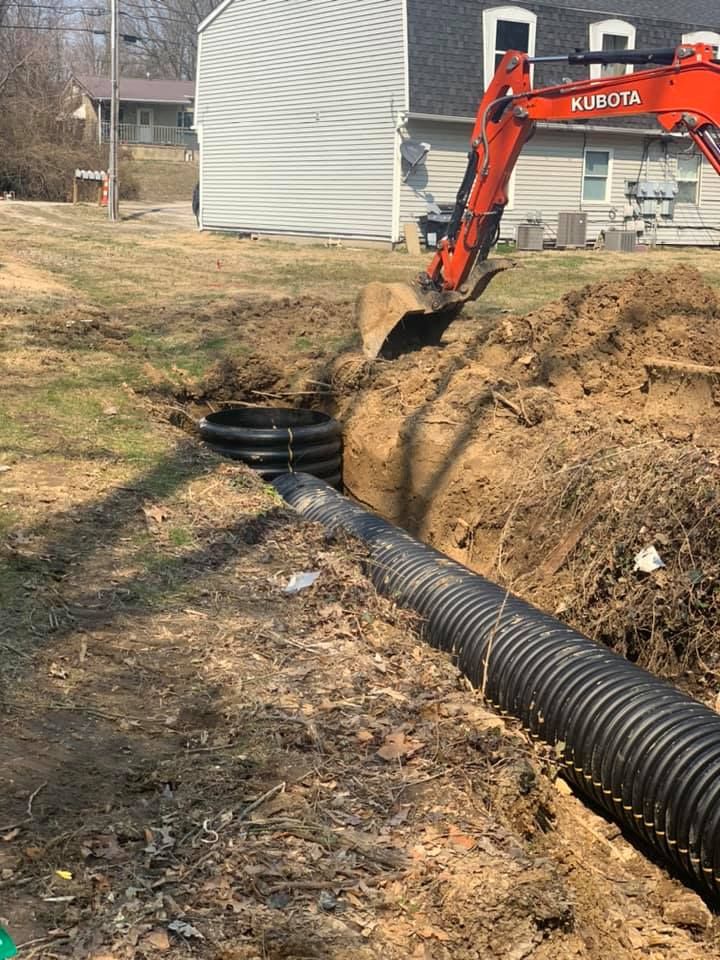 Excavator digging a trench for drainage pipe in a yard.