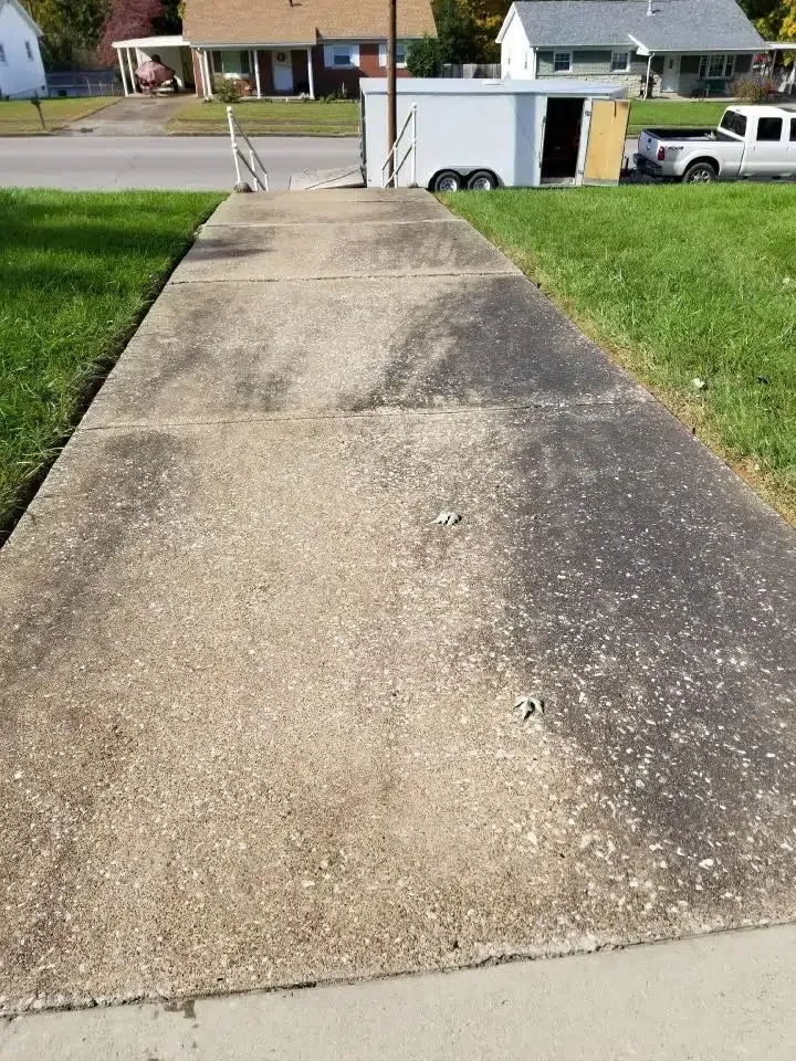 Concrete sidewalk, half cleaned, shows before and after pressure washing, grass on either side.