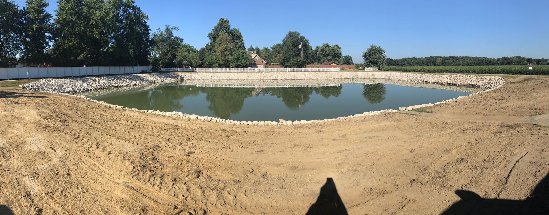 A pond surrounded by rocks and dirt under a clear blue sky, with trees in the background.