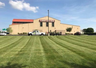 A Furniture Row store with a freshly mowed lawn. A truck with a trailer are parked in front of the building.
