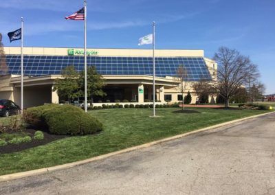 Holiday Inn hotel exterior with flags on a sunny day. Green grass and landscaping in front.