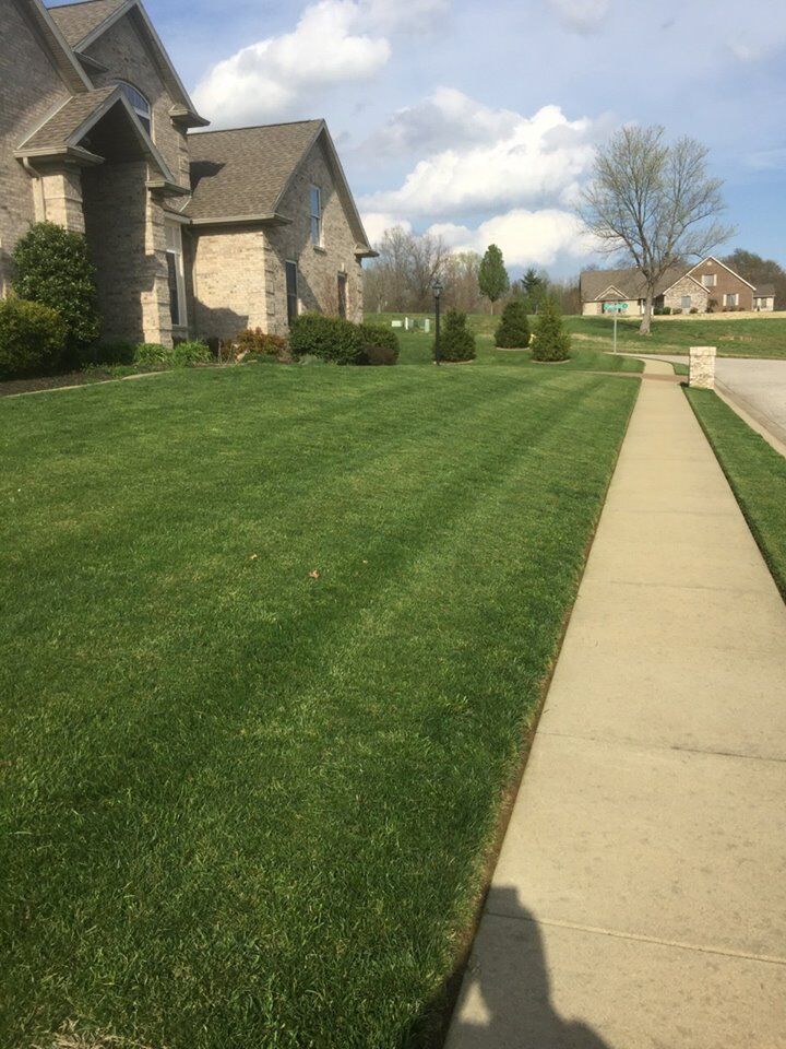 Lawn with striped pattern next to a sidewalk and a two-story brick house on a sunny day.