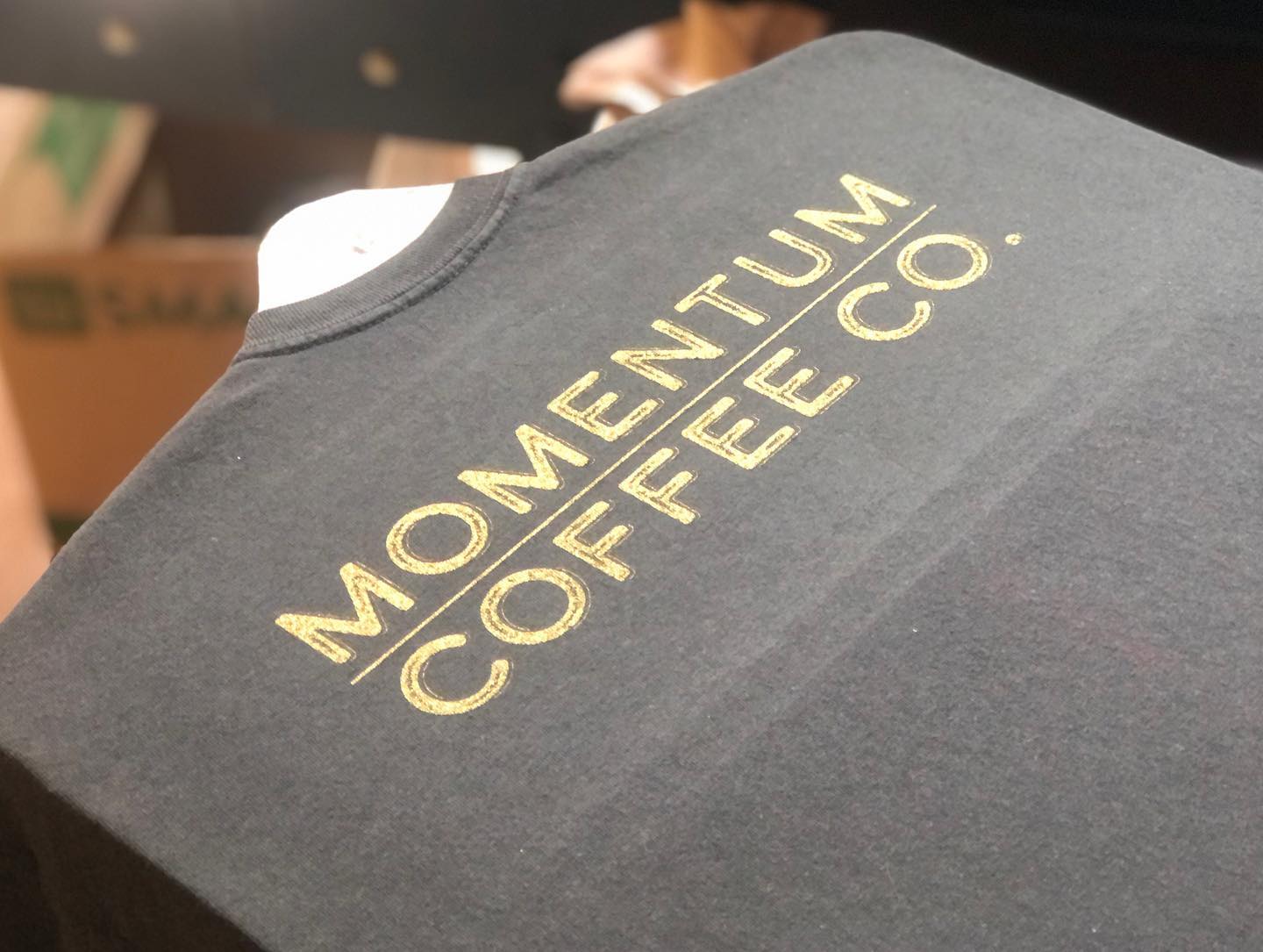 a black momentum coffee co. t-shirt is hanging on a hanger