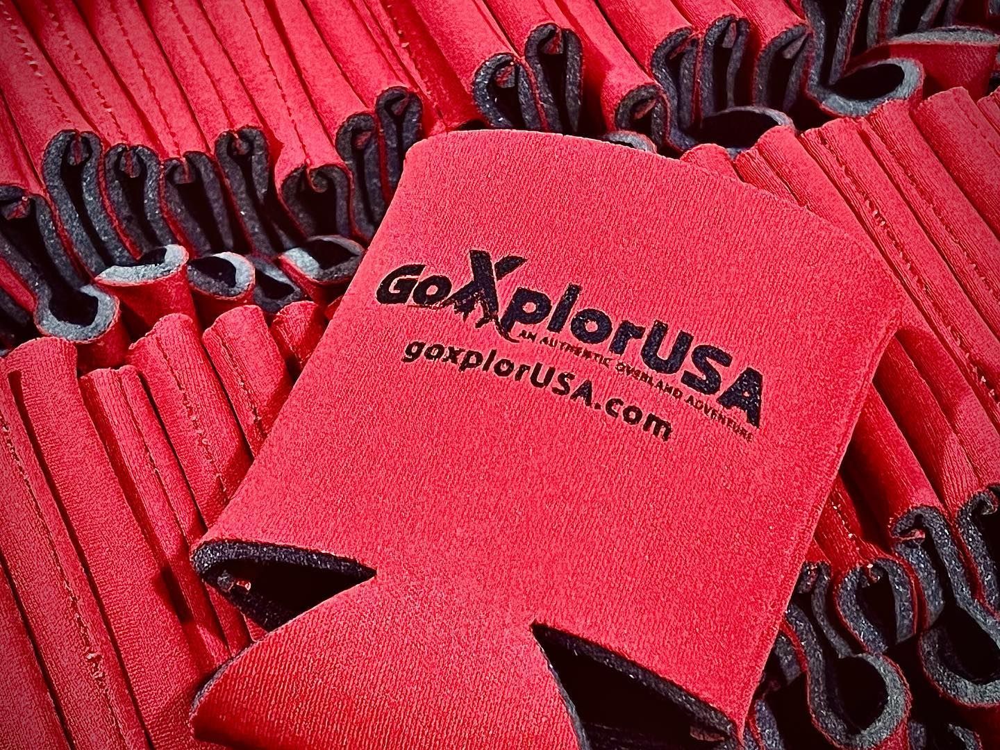 a red can holder with the word go explore usa on it is sitting on top of a pile of red can holders .
