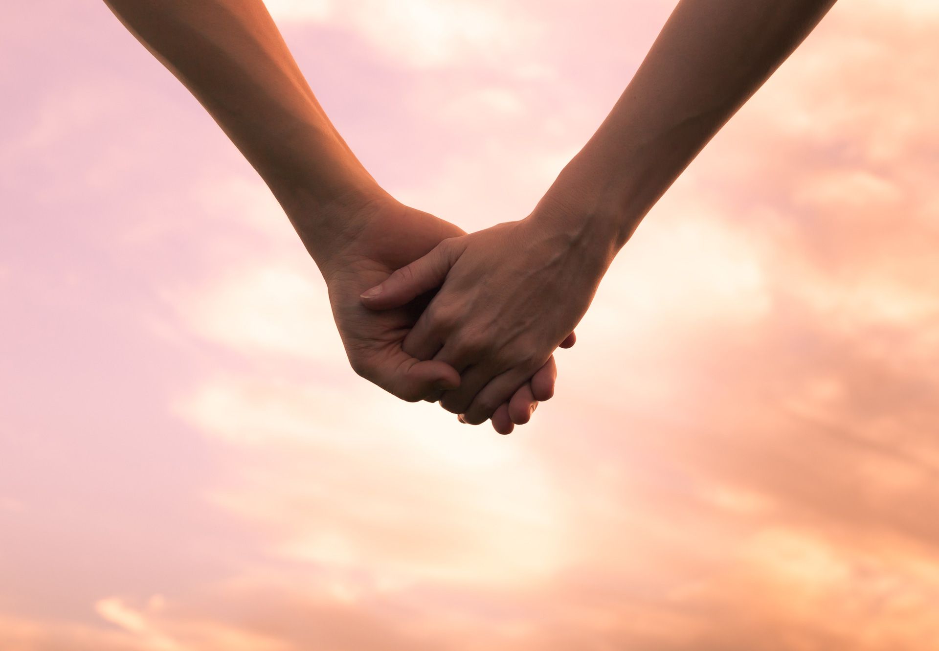 Two people are holding hands in front of a cloudy sky.