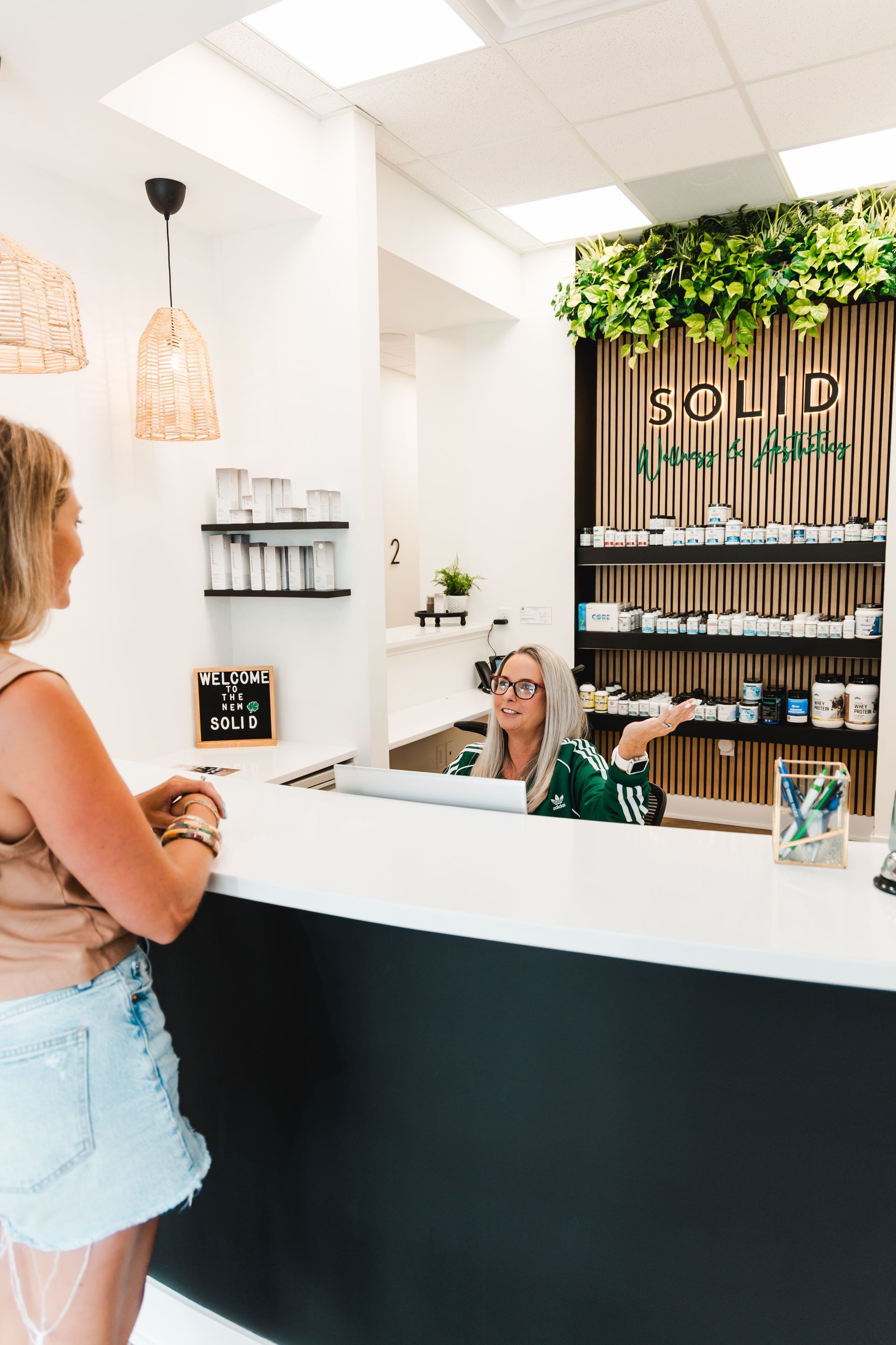 Woman at shop counter talking to a person. Green-themed dispensary with products on display.