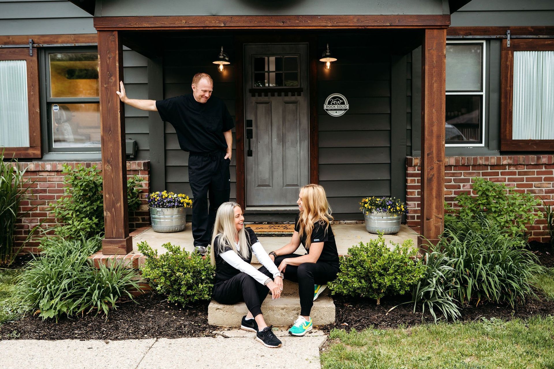 A man and two women are sitting on the porch of a house.