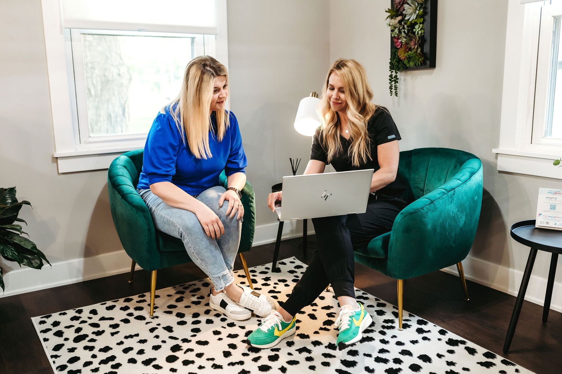 Two women are sitting in green chairs looking at a laptop.