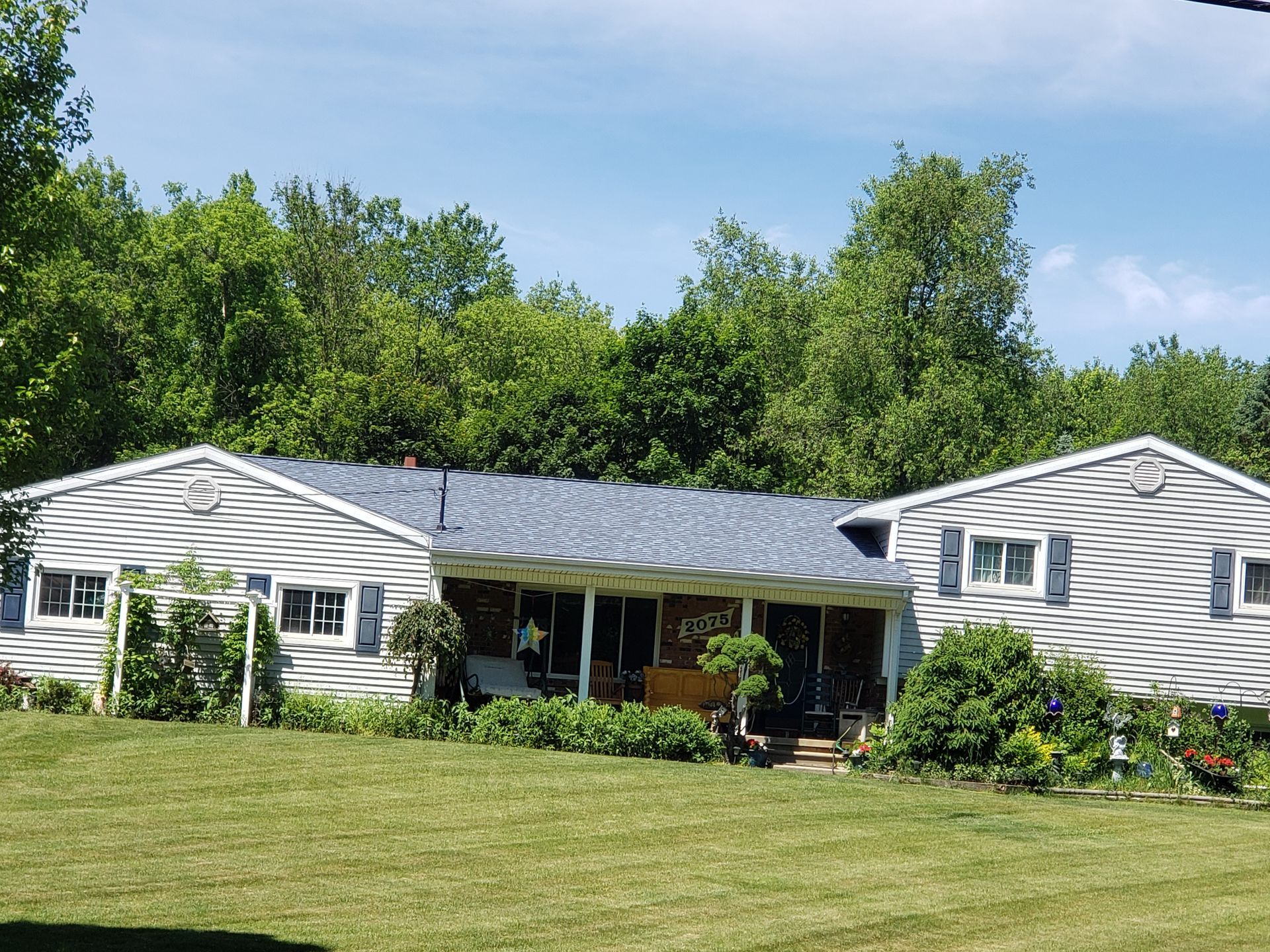 A white house with a blue roof sits in the middle of a lush green field