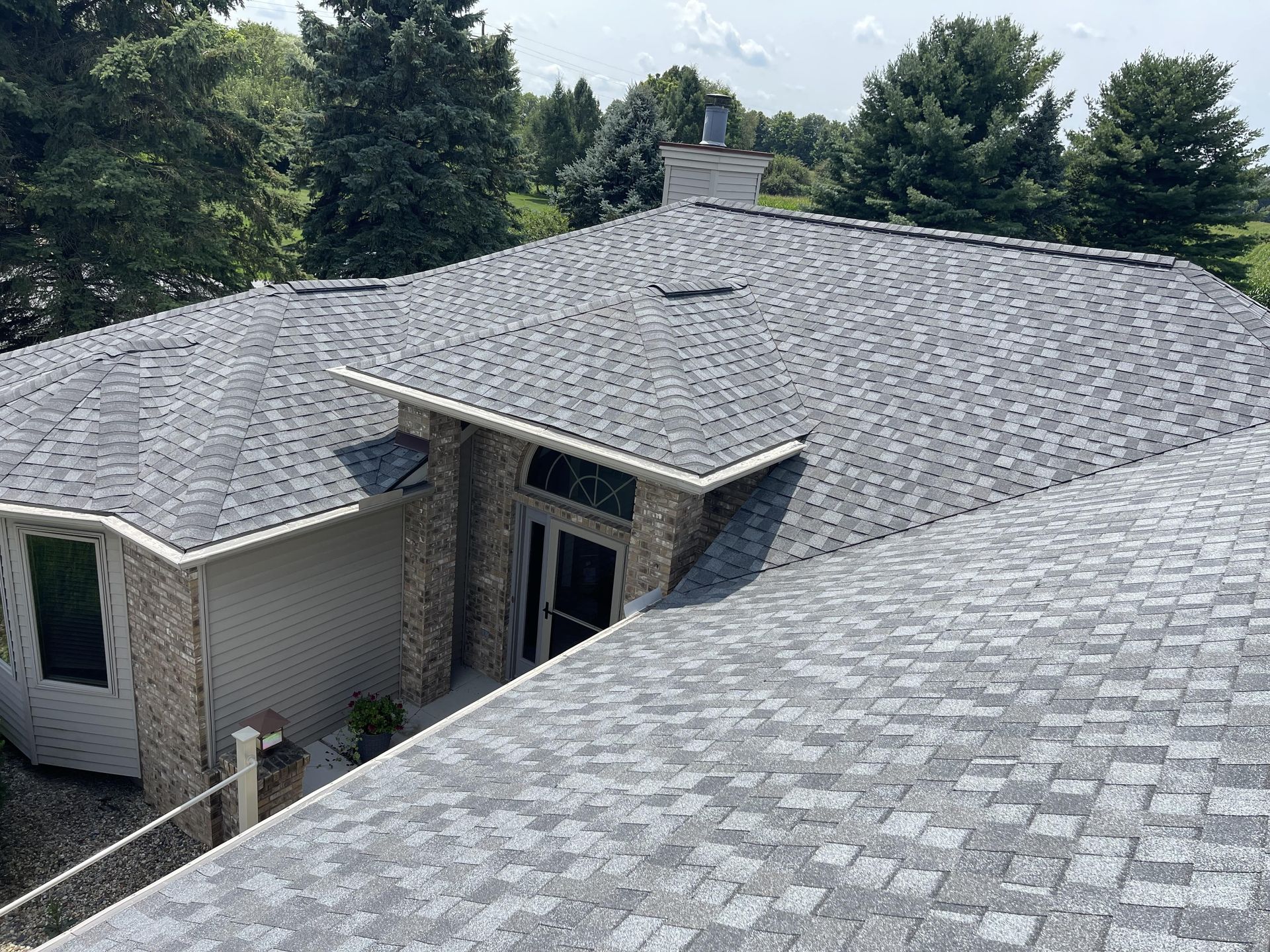 An aerial view of a house with a gray roof and trees in the background.
