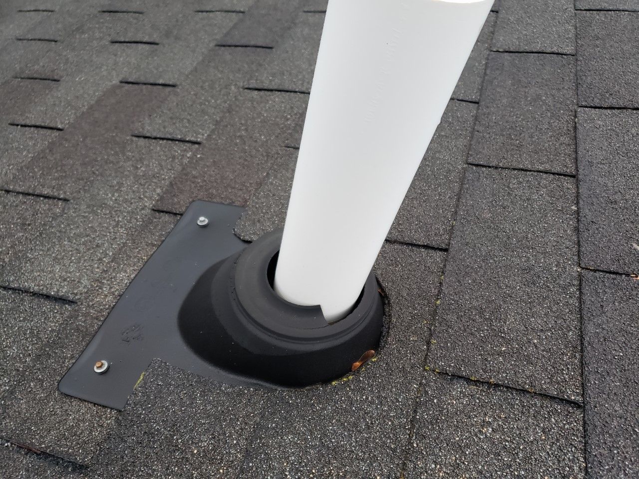 A white pipe is sticking out of a hole in a roof