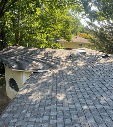 The roof of a house with a gray shingle roof is surrounded by trees.