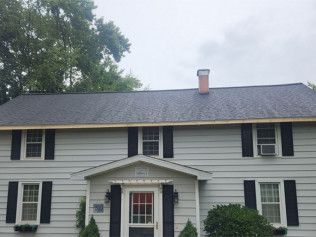 A white house with black shutters and a chimney on the roof.